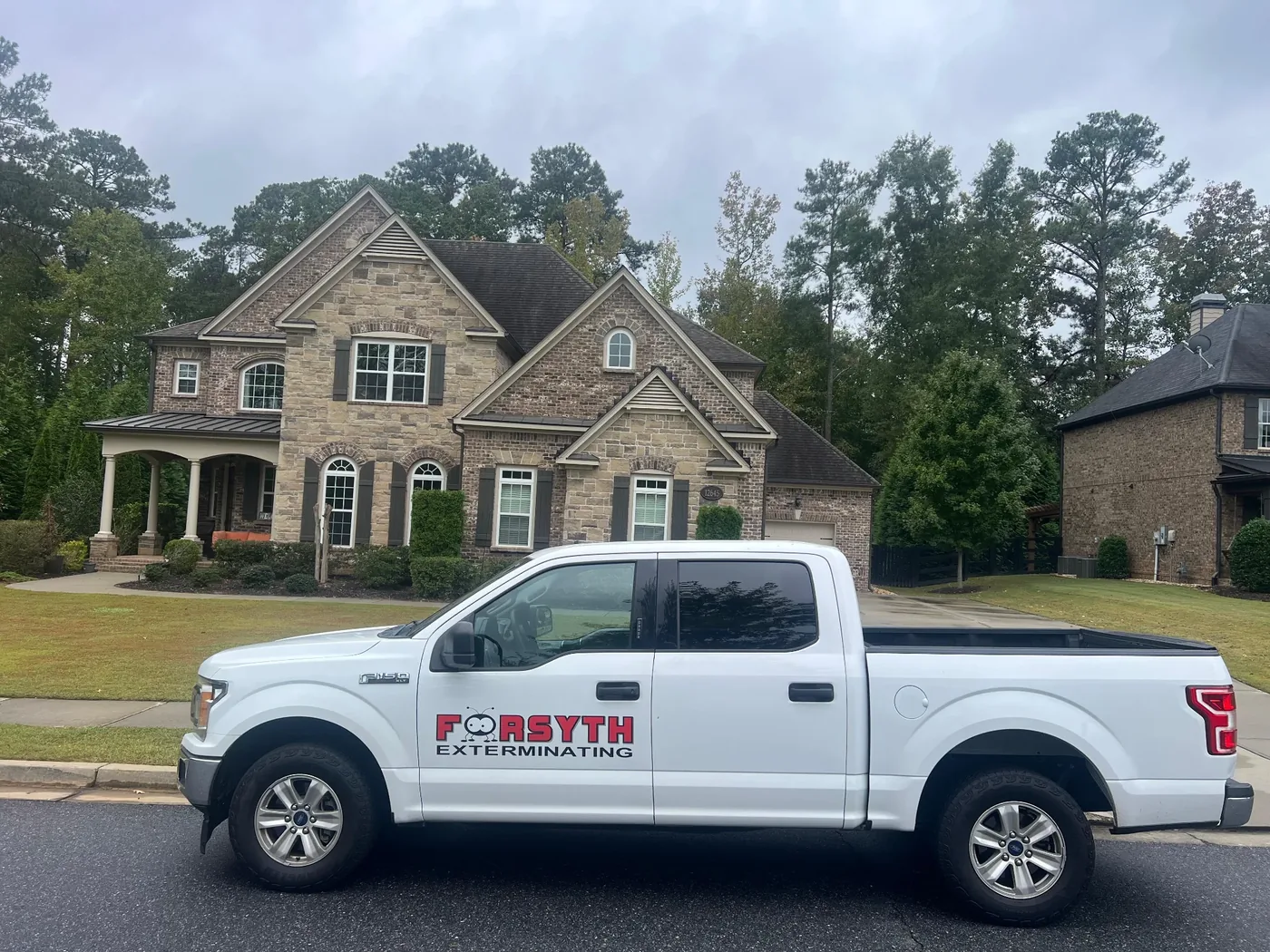 A white Forsyth Exterminating service truck parked in front of a house